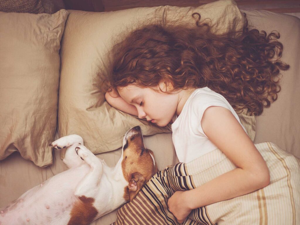little girl laying in bed with a small dog
